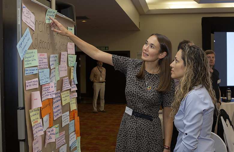 Teilnehmende aus Costa Rica und Deutschland stehen vor der Metaplanwand mit dem Themenspeicher und besprechen die Aufnahme weiterer für sie relevante Themen
